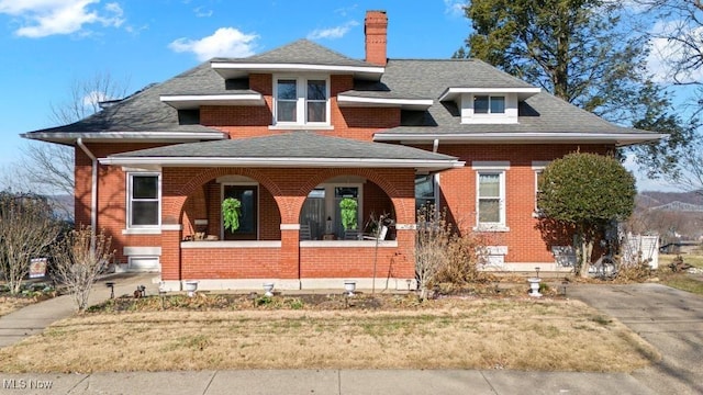 bungalow-style home featuring a shingled roof, covered porch, brick siding, and a chimney