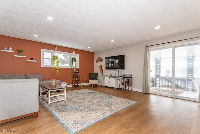 living room featuring recessed lighting, baseboards, a textured ceiling, and light wood-style flooring