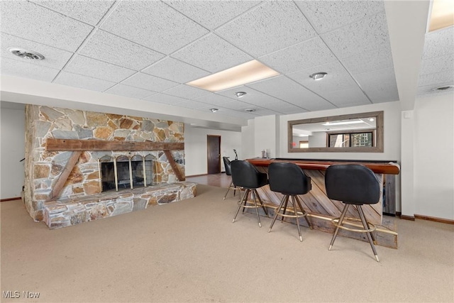 interior space featuring visible vents, a stone fireplace, a paneled ceiling, a dry bar, and carpet flooring