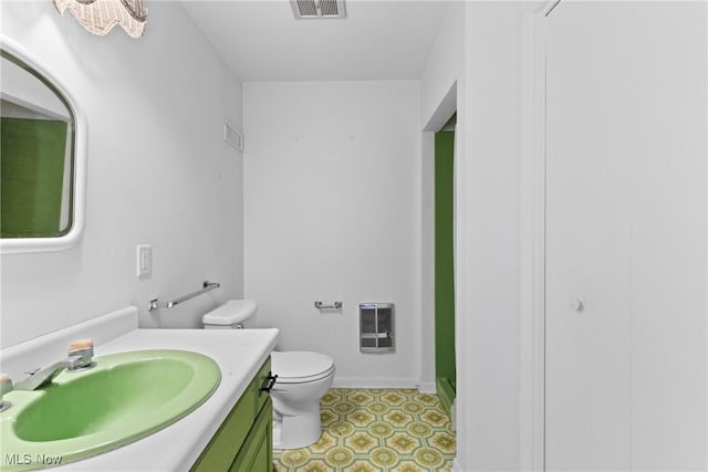 bathroom with vanity, heating unit, visible vents, baseboards, and toilet