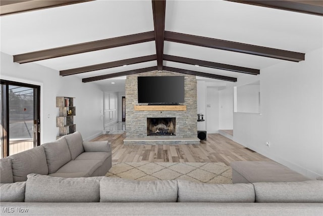 living area with visible vents, a stone fireplace, vaulted ceiling with beams, and light wood finished floors