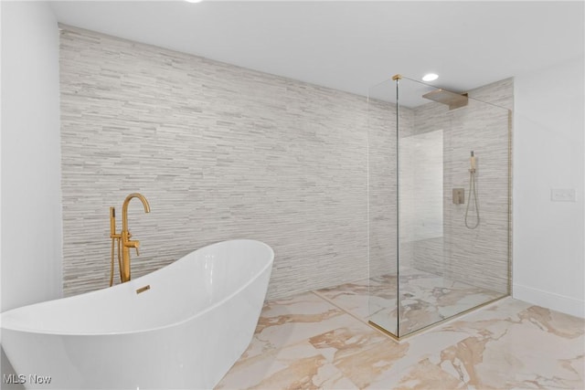 full bath featuring tile walls, a freestanding tub, a walk in shower, and marble finish floor