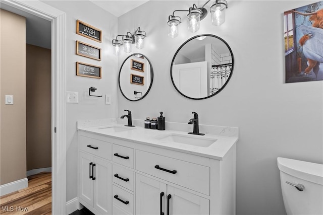 full bathroom with double vanity, toilet, wood finished floors, and a sink