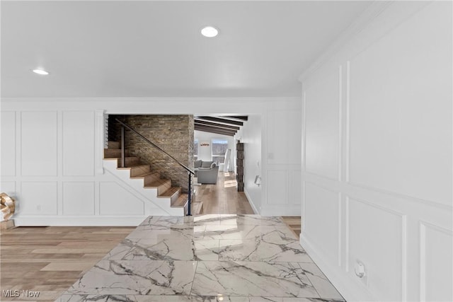 interior space featuring a decorative wall, stairs, light wood-style floors, and ornamental molding