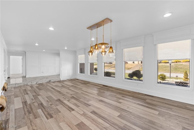 unfurnished living room with recessed lighting, light wood-style floors, a notable chandelier, and a decorative wall