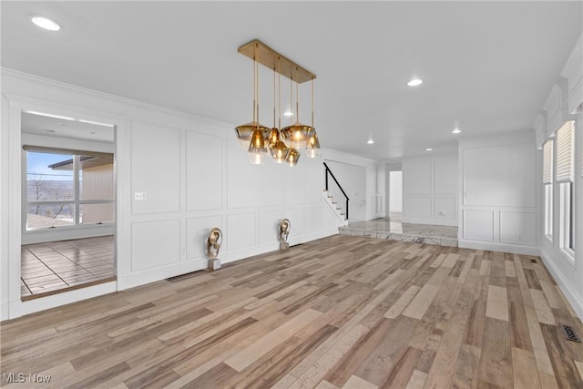 unfurnished living room with crown molding, a decorative wall, and light wood-style floors