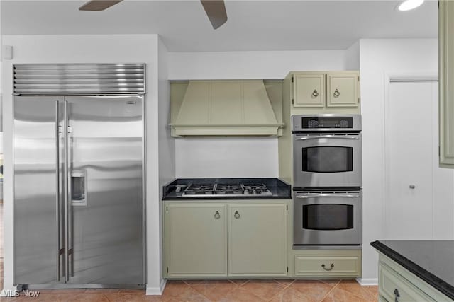 kitchen featuring premium range hood, light tile patterned flooring, stainless steel appliances, a ceiling fan, and green cabinetry