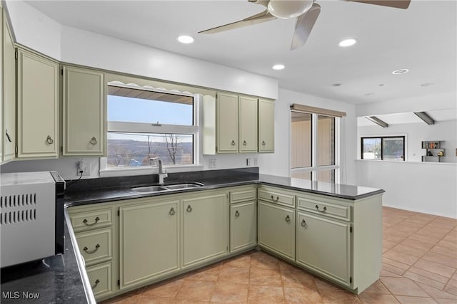 kitchen with recessed lighting, a peninsula, green cabinets, and a sink