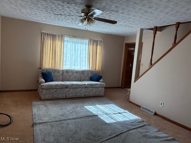 carpeted living room with visible vents, a textured ceiling, baseboards, and a ceiling fan