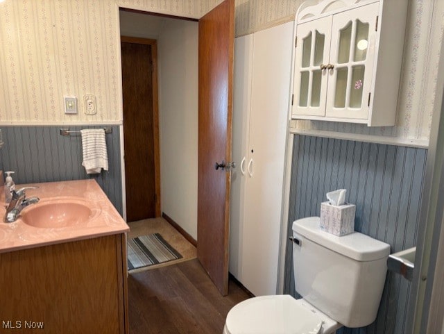 bathroom with toilet, a sink, wood finished floors, wainscoting, and wallpapered walls