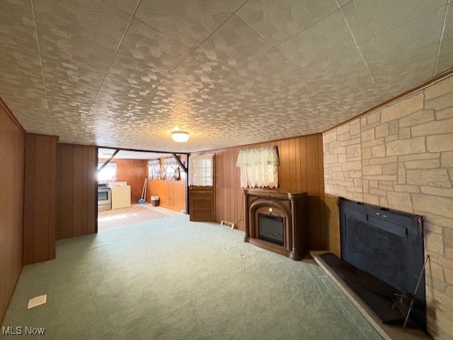 unfurnished living room with carpet, wood walls, and a fireplace