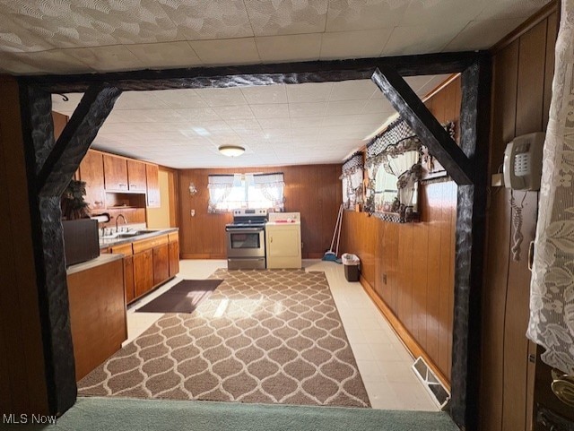 kitchen with electric range, a sink, washer / clothes dryer, wooden walls, and light countertops