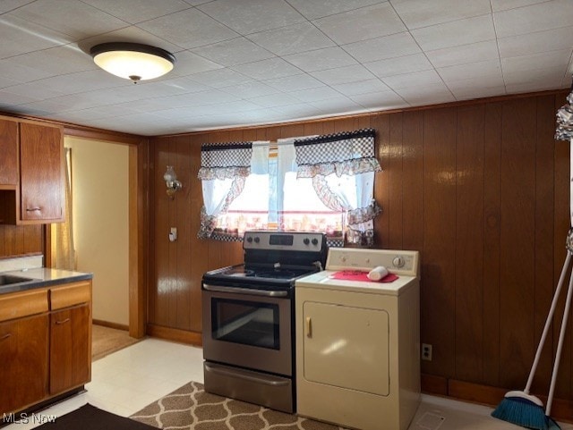 kitchen with light floors, washer / dryer, stainless steel range with electric stovetop, wood walls, and brown cabinets