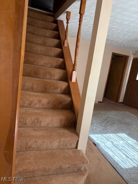 staircase featuring carpet floors and a textured ceiling