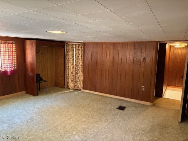 carpeted empty room featuring visible vents and wooden walls