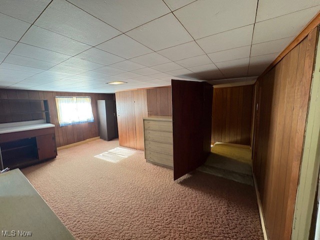 basement with a drop ceiling, carpet, and wooden walls