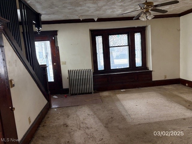 foyer featuring radiator, crown molding, baseboards, ceiling fan, and stairs