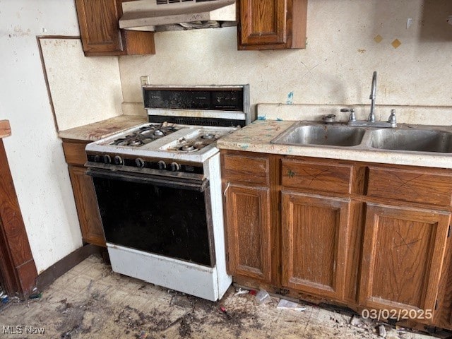 kitchen featuring under cabinet range hood, light countertops, white gas range, brown cabinets, and a sink