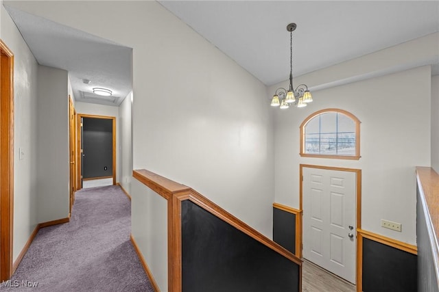 corridor featuring vaulted ceiling, a notable chandelier, light colored carpet, and baseboards