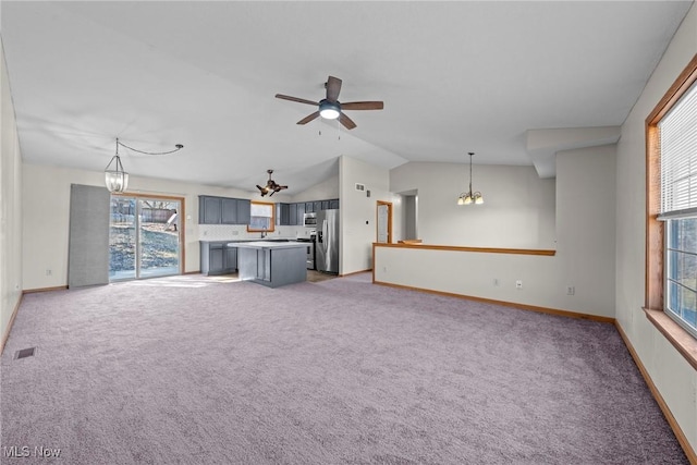 unfurnished living room with visible vents, lofted ceiling, light colored carpet, and ceiling fan with notable chandelier