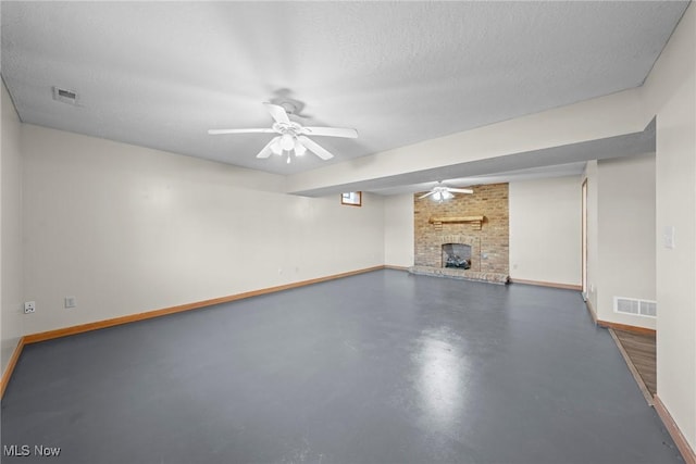 finished basement featuring visible vents, a fireplace, a textured ceiling, and a ceiling fan