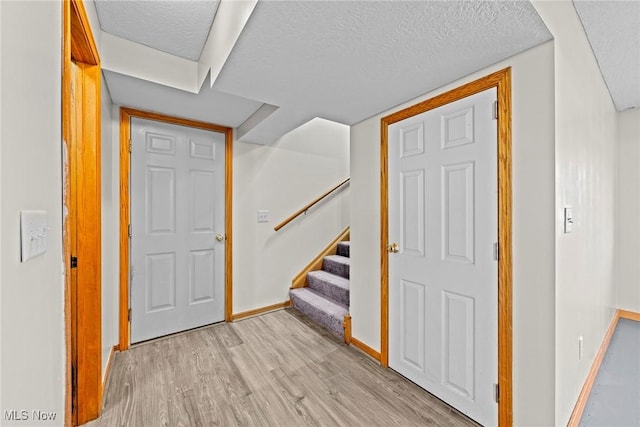 foyer featuring stairway, baseboards, light wood-style floors, and a textured ceiling