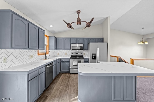 kitchen featuring light stone countertops, a sink, vaulted ceiling, appliances with stainless steel finishes, and pendant lighting