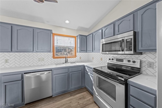 kitchen with vaulted ceiling, decorative backsplash, light wood-style flooring, appliances with stainless steel finishes, and a sink