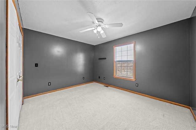 carpeted spare room featuring a textured ceiling, visible vents, baseboards, and ceiling fan