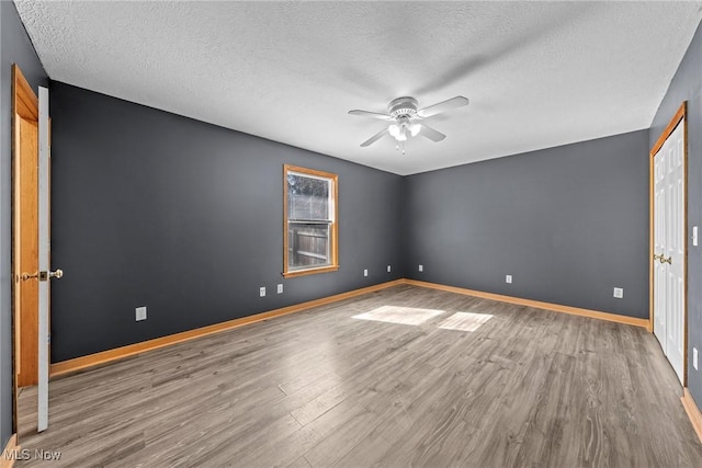 empty room featuring ceiling fan, baseboards, a textured ceiling, and wood finished floors