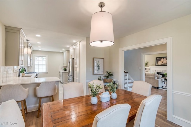 dining area featuring recessed lighting, a fireplace, wood finished floors, and stairs