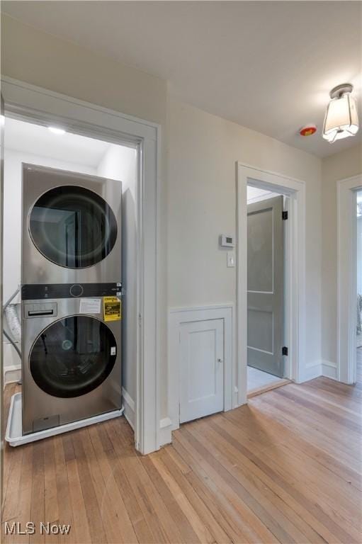 clothes washing area featuring stacked washer / drying machine, baseboards, wood finished floors, and laundry area