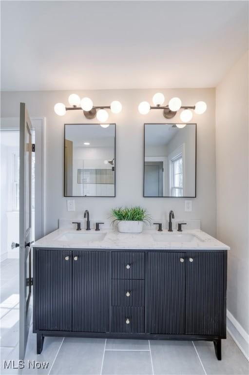 full bath with double vanity, tile patterned flooring, baseboards, and a sink