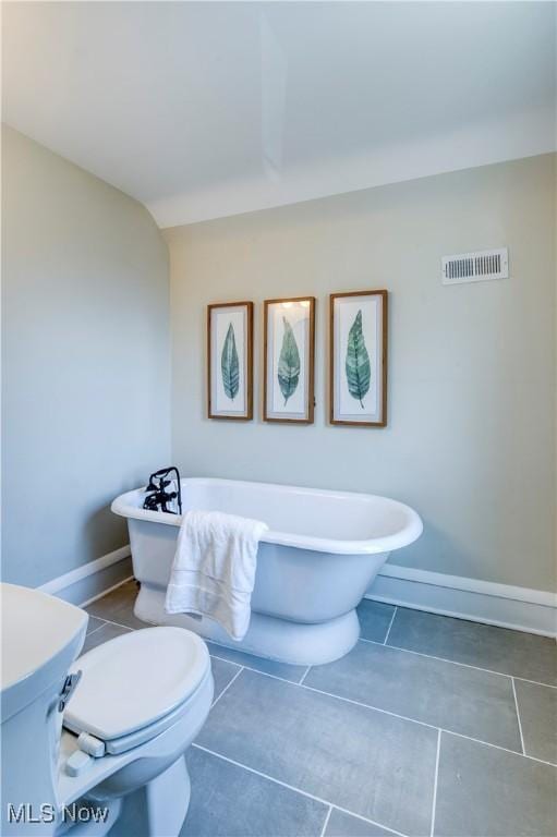 bathroom with visible vents, baseboards, toilet, and a freestanding bath