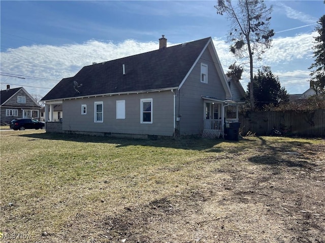 back of house featuring a lawn, fence, roof with shingles, and a chimney