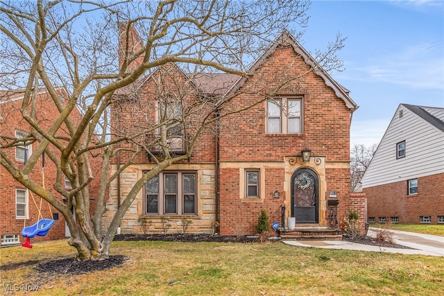 tudor-style house with stone siding, brick siding, and a front yard