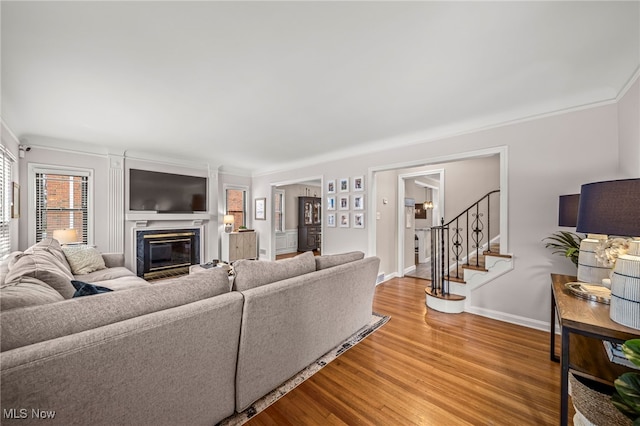 living area featuring light wood-style flooring, ornamental molding, a glass covered fireplace, baseboards, and stairs