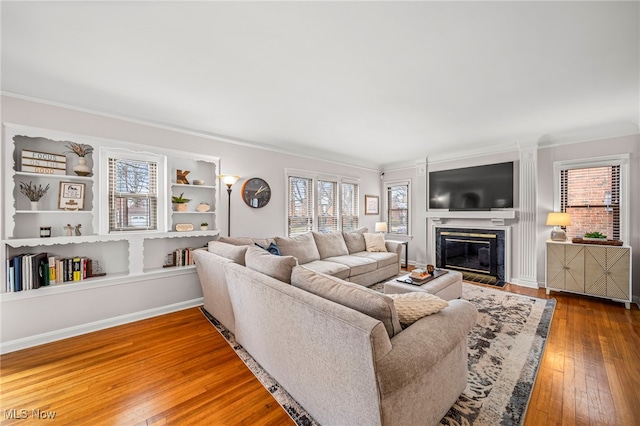 living area featuring baseboards, wood-type flooring, ornamental molding, and a high end fireplace