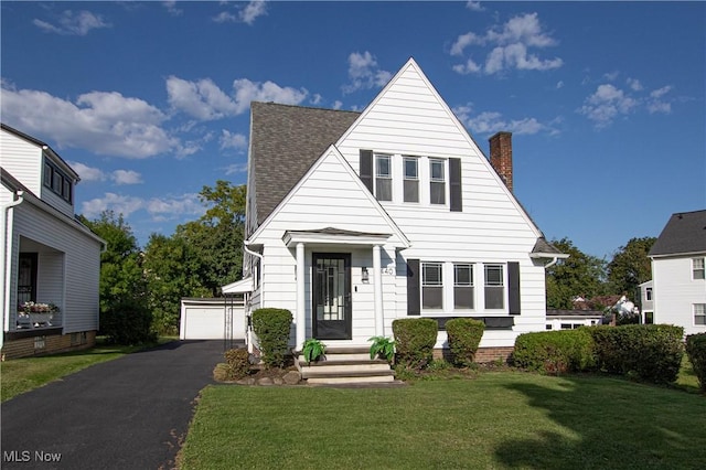 view of front of house featuring roof with shingles, a chimney, an outdoor structure, a front lawn, and a detached garage