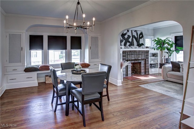 dining space with wood finished floors, a fireplace, arched walkways, crown molding, and a notable chandelier