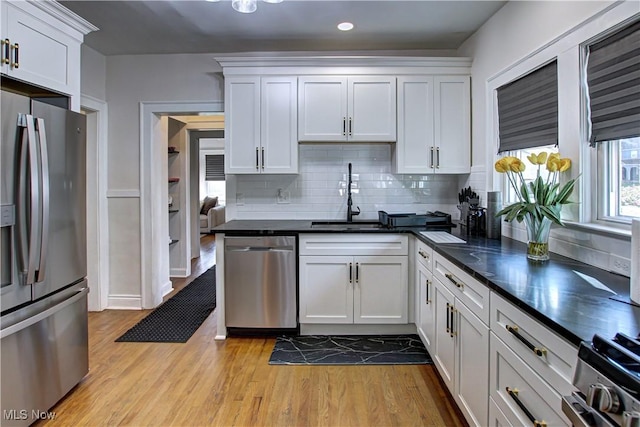 kitchen with light wood-type flooring, a sink, dark countertops, appliances with stainless steel finishes, and white cabinets