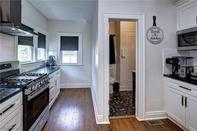 kitchen with dark wood finished floors, dark countertops, wall chimney exhaust hood, and stainless steel appliances