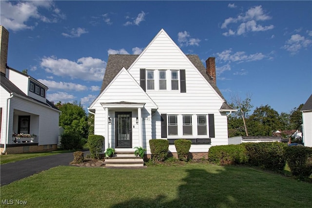 bungalow with driveway, a chimney, a front yard, and a shingled roof