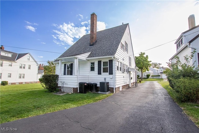 view of front of house with central AC unit, a chimney, a front yard, and a shingled roof