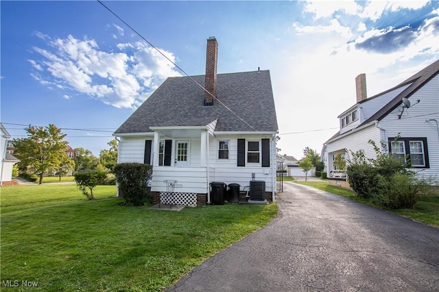 back of property featuring a lawn, a chimney, central AC, and a shingled roof