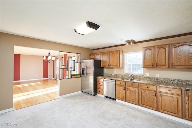 kitchen featuring a sink, appliances with stainless steel finishes, brown cabinetry, baseboards, and light stone countertops