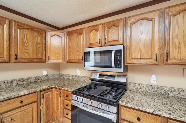 kitchen with light stone countertops, a textured ceiling, appliances with stainless steel finishes, and brown cabinets