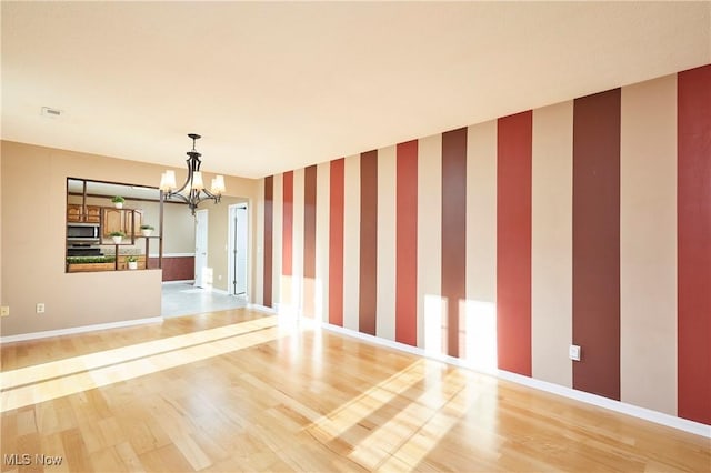 empty room featuring wallpapered walls, an accent wall, baseboards, a chandelier, and light wood-type flooring