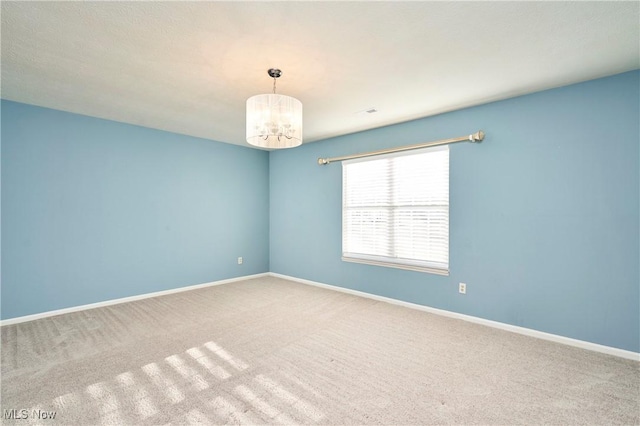 carpeted spare room featuring baseboards and a chandelier