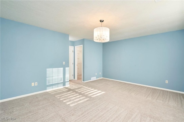 carpeted spare room with a chandelier, visible vents, a textured ceiling, and baseboards